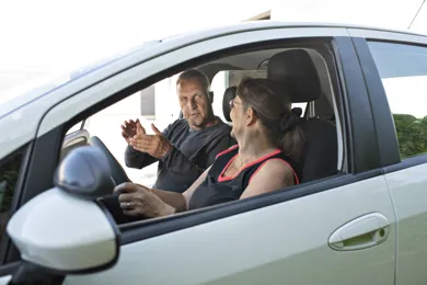 En kvinde sidder i en bil og faar vejledning af en koerelaerer.