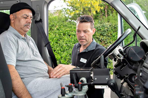 En borger sidder i en specialindrettet bil, mens en ansat i HandicapBilistCentret hjælper til. HandicapBilistCentret er uvildig og vælger altid billigst egnet bil til borgere med handicap.